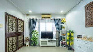 A living room with a TV, white cabinets, a potted plant, and a decorative wall piece. - Spacious 3BR Private House Near Old City Near Night Bazaar (Muang Chiang Mai)