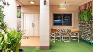 A covered outdoor area with a door, artificial grass, two white chairs, and a window. - Spacious 3BR Private House Near Old City Near Night Bazaar (Muang Chiang Mai)