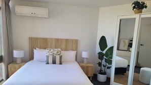 A neatly arranged hotel room with a large bed, two bedside tables with lamps, a potted plant, a mirror, and a wardrobe. - Centreport Units (Portland)