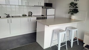 A modern kitchen with white cabinets, a microwave, a refrigerator, a coffee maker, and two white bar stools. - Centreport Units (Portland)