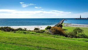 A coastal landscape with a grassy area, a road leading to a pier, and a distant industrial structure. - Centreport Units (Portland)