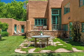 Un patio con una mesa redonda y sillas, un muro de piedra y un pequeño jardín.