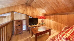 Un interior de madera con televisión, lámpara, muebles de mimbre y una manta de cuadros.