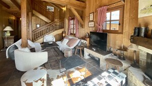 Acogedor interior de una cabaña de madera con chimenea, asientos cómodos y una escalera.