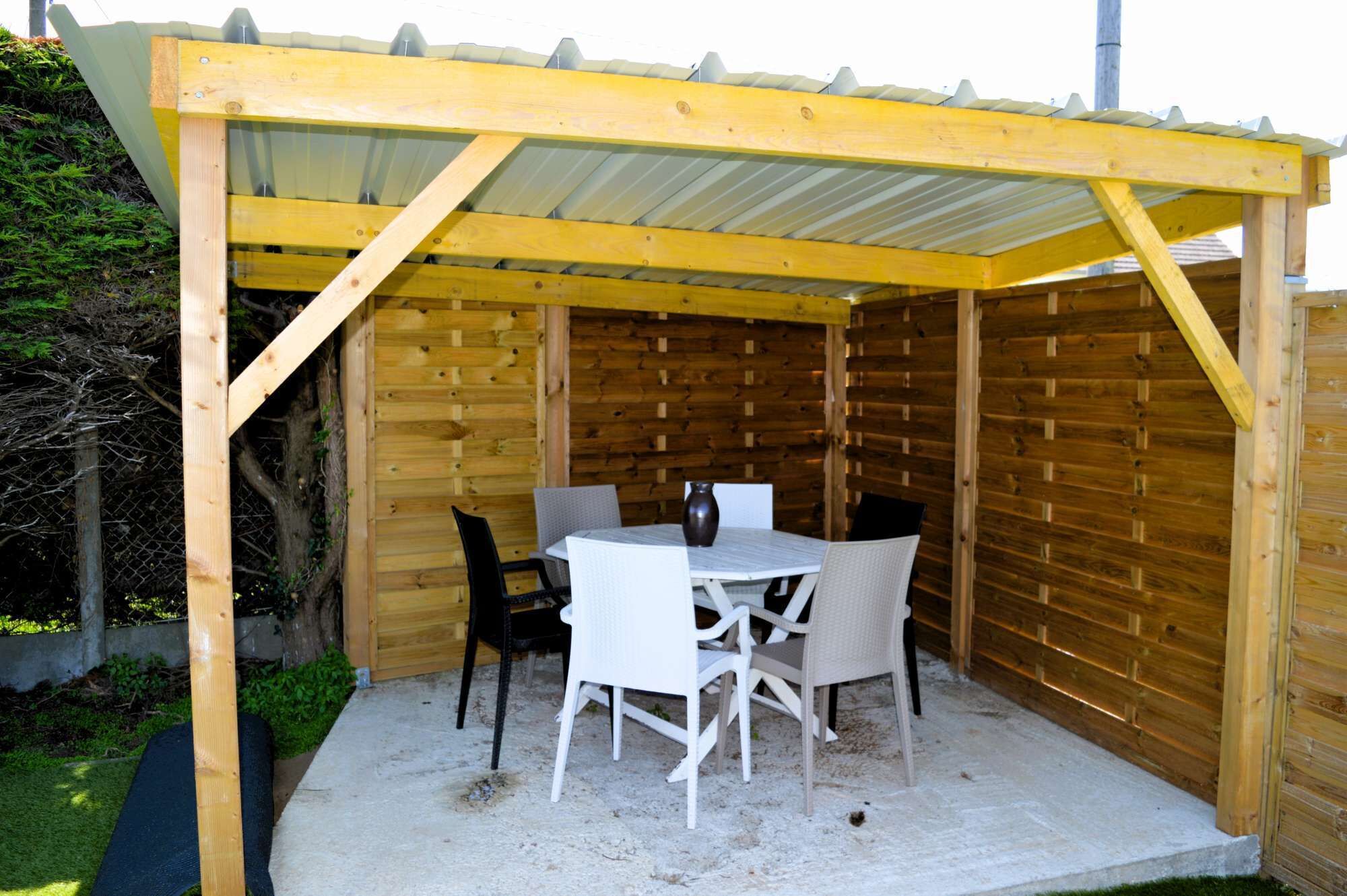 En overdækket terrasse med et træbord og stole, omgivet af trævægge.