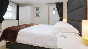 A hotel room with a bed, a bedside table with a lamp, a wardrobe, a window with curtains, and a door with an exit sign.