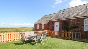 A brick cottage with a fenced patio, a table with chairs, and a view of the countryside.