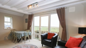 A cozy living room with a black leather sofa, a dining table with chairs, and a large window with curtains.