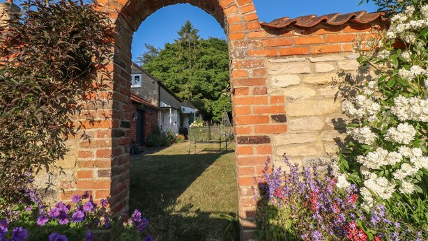 Um arco de tijolos que leva a uma casa com jardim à frente.