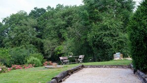 A billiards table in a garden with a table and chairs, surrounded by greenery.