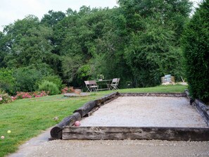 Une table de billard dans un jardin, avec une table et des chaises, le tout entouré de verdure.