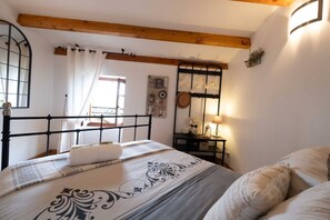 A bedroom with a bed, a bedside table with a lamp, a mirror, and a window with curtains. - L'Écrin du Puech - Pool & SPA - Gym room (Teillet)