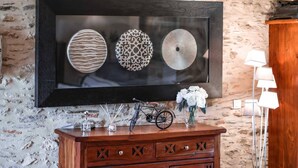 A framed artwork of three decorative plates on a wall. Below, a wooden cabinet with decorative cutouts and a bicycle.