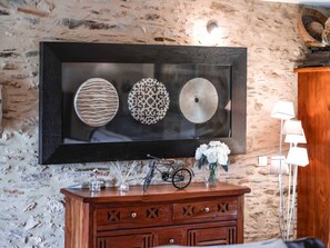 Une œuvre d’art encadrée représentant trois assiettes décoratives accrochées à un mur. En dessous, un meuble en bois orné de motifs découpés et un vélo.