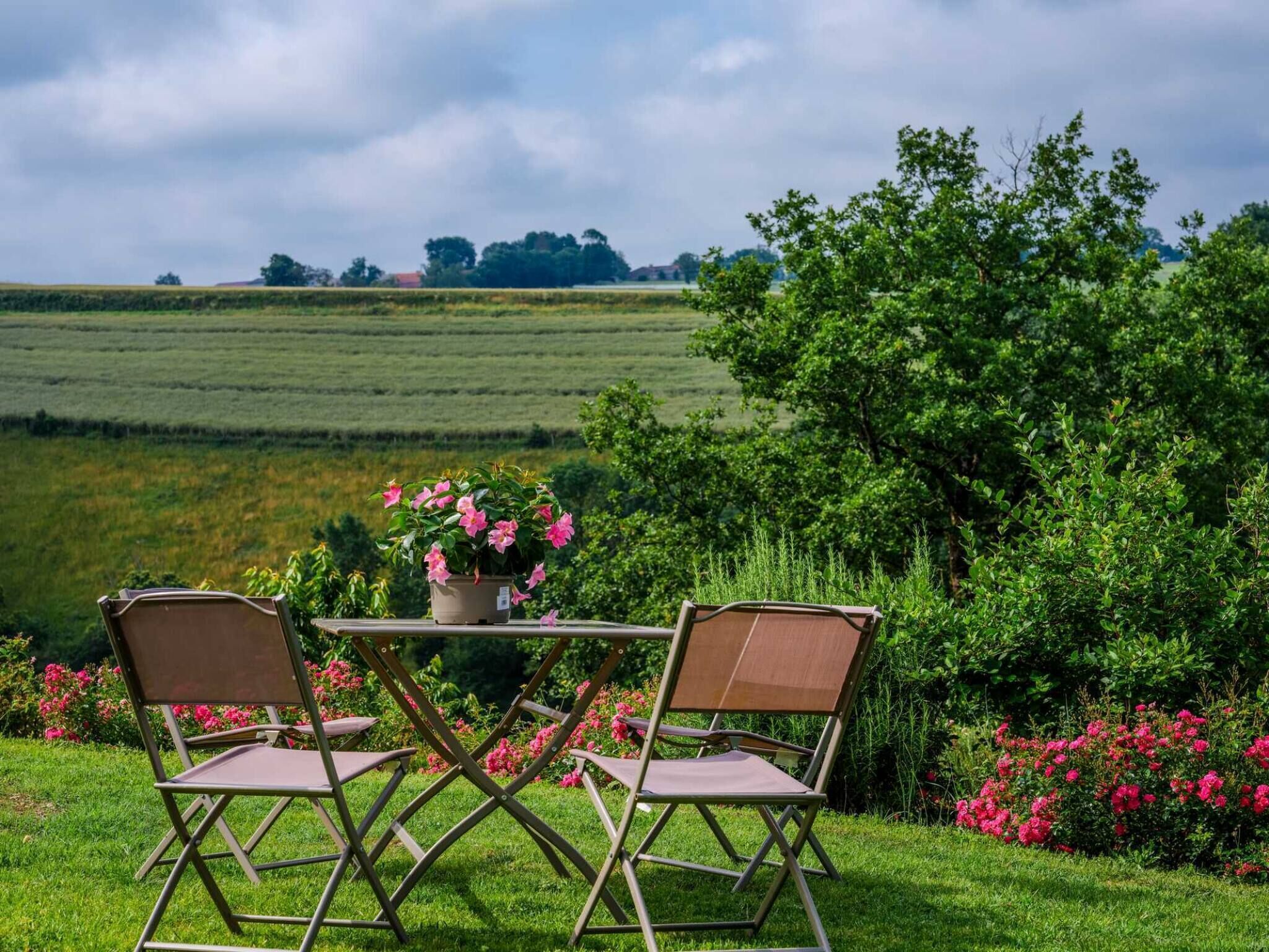 A table with two chairs in a garden with a view of a field and trees.