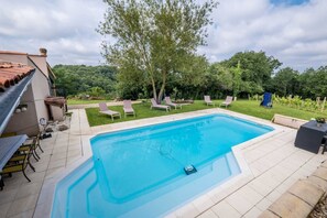 A rectangular swimming pool with a tiled deck, surrounded by a grassy area with lounge chairs and a tree.