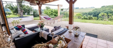 An outdoor seating area with wicker furniture, a hammock, and a view of the countryside.