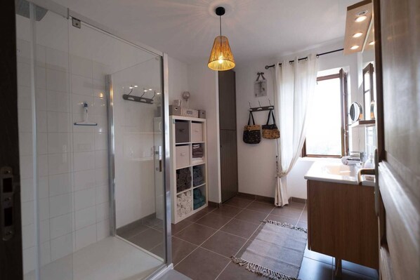 A modern bathroom with a glass shower enclosure, a vanity with a mirror, and a hanging light fixture.