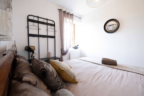 Une chambre à coucher avec un lit, une table de chevet, un miroir et une fenêtre avec des rideaux.
