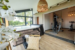 Une chambre moderne dotée d’un jacuzzi, d’appareils de musculation et de grandes fenêtres donnant sur un paysage verdoyant.