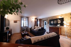 Un salon avec un canapé, une table basse, un téléviseur, une cheminée et un mur en pierre.