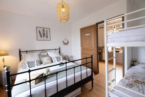 A bedroom with a black metal bed frame, a white mattress, and a bedside table with a lamp. There is a wooden door and a white bunk bed in the background. - L'Écrin du Puech - Pool & SPA - Gym room (Teillet)