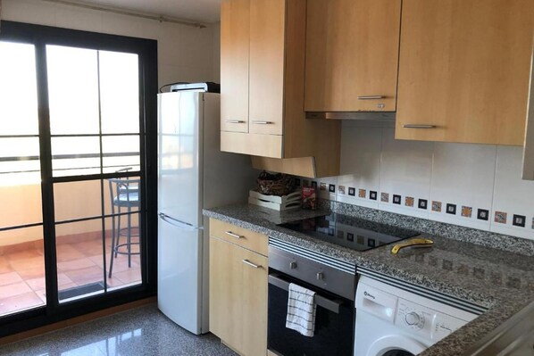 Una cocina con armarios de madera, horno empotrado, lavavajillas y un amplio ventanal con vistas al exterior.