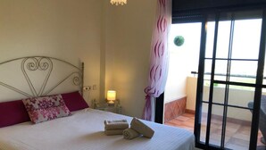 A hotel room with a bed, a nightstand with a lamp, a window with a curtain, and a view of the outside.