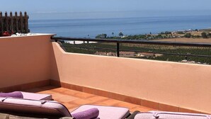 A balcony with a view of the sea, a wooden fence, and a few lounge chairs.