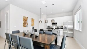 A modern kitchen with stainless steel appliances, a dining area with a wooden table and chairs, and pendant lighting.