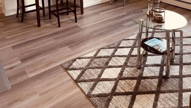 A room with a dining table set for two, a small round table with a glass top, a flat-screen TV mounted on the wall, and a window with curtains. - North Star Place Apt 12 (Fairbanks)