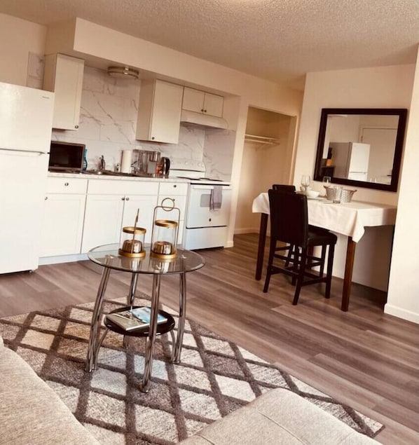 A modern kitchen with white cabinets, a dining area with a glass table, and a small mirror above the counter.