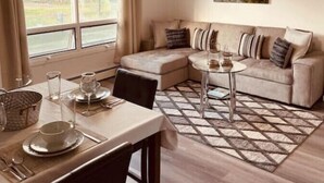 A cozy living room with a sofa, a dining table set with glasses, and a painting on the wall. - North Star Place Apt 12 (Fairbanks)