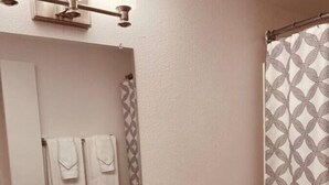 A bathroom with a white sink, two faucets, a mirror, a towel rack with two towels, a shower curtain with a geometric pattern, and a bottle of orange liquid on the counter. - North Star Place Apt 12 (Fairbanks)