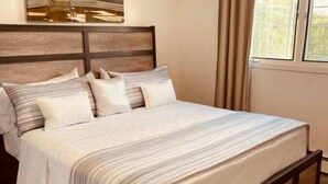 A bedroom with a large bed, a headboard, a window with curtains, and a painting on the wall. - North Star Place Apt 12 (Fairbanks)