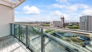 Un balcone con ringhiera in vetro che si affaccia su una vista urbana, con un edificio rosso caratteristico e palazzi moderni.