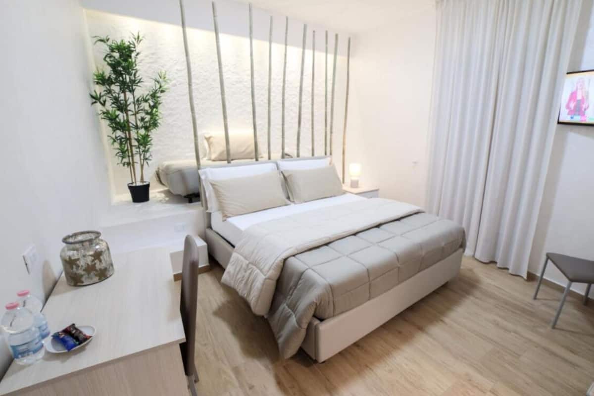 A modern bedroom with a bed, bedside table, lamp, and a potted plant.