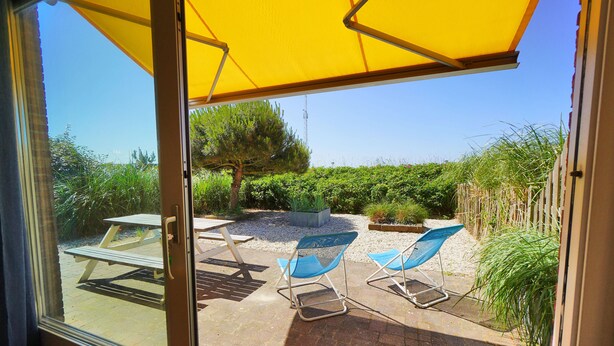 Eine Terrasse im Freien mit Picknicktisch und blauen Stühlen unter einem gelben Sonnenschirm.