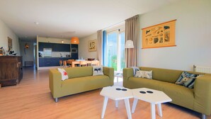 Ein modernes Wohnzimmer mit einer Couch, zwei Couchtischen und einer Küche im Hintergrund.