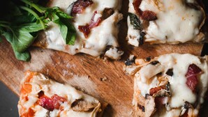 A wooden cutting board with four pieces of pizza topped with cheese, mushrooms, and bacon. - Roomshala 080 Hotel Kings (New Delhi)