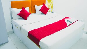 A neatly made bed with a red blanket, white pillows, and a red and white striped pillow. - Roomshala 080 Hotel Kings (New Delhi)