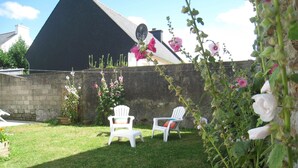 Un jardín con dos sillas blancas, un muro de piedra y un edificio con techo negro.