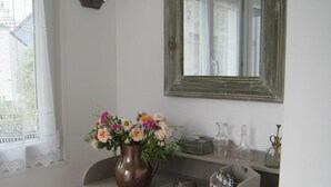 Un baño con tocador de madera, espejo, un florero con flores y varios artículos de tocador.