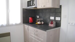 Cocina equipada con microondas, hervidor de agua y un refrigerador pequeño. Hay armarios y una encimera.