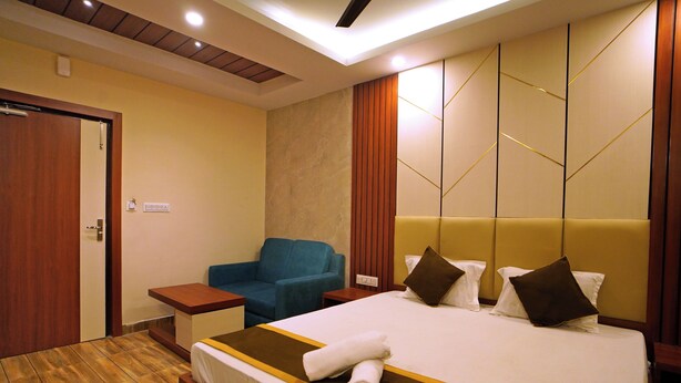 A hotel room with a bed, a blue armchair, a wooden floor, and a wooden headboard. - Royal Sea View (Kanthi)