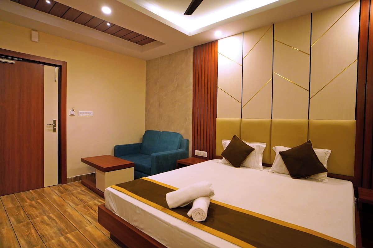 Habitación de hotel con una cama, un sillón azul, suelo de madera y cabecero de madera.