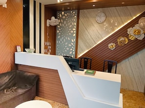 A reception desk with a modern design, a wooden accent wall, and a decorative panel with leaf cutouts. - Royal Sea View (Kanthi)