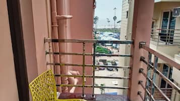 A balcony with a metal railing, a yellow chair, and a view of a parking area with cars and a building in the background.