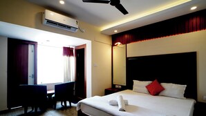 A hotel room with a bed, a desk, a chair, an air conditioner, and a ceiling fan. - Royal Sea View (Kanthi)