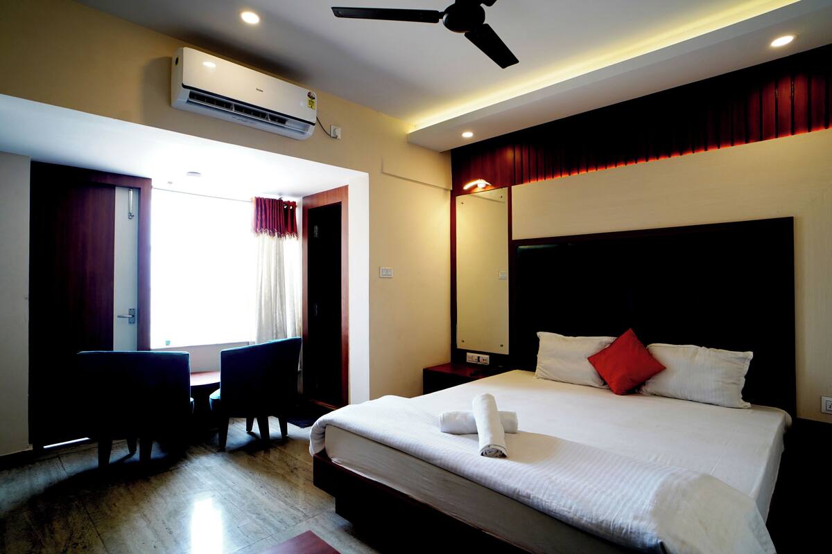 Habitación de hotel con cama, escritorio, silla, aire acondicionado y ventilador de techo.